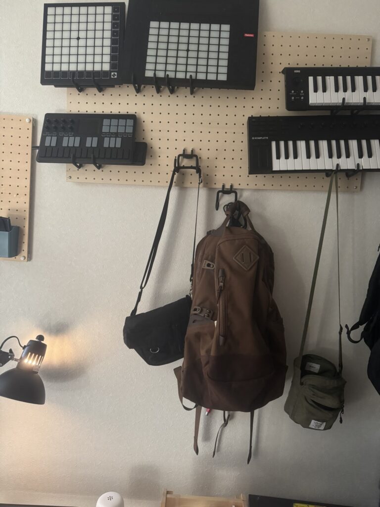 白い有孔ボードに掛けたvisvim BALLISTIC 20Lの茶色いバックパック